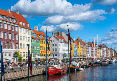 Kopenhag, Danimarka - 13 Eylül 2010: İkonik Nyhavn restoran cepheleri mavi bulutlar altında parlak renklerde. İnsanlar yürüyor ve oturuyor. Kanal suyunda tekneler