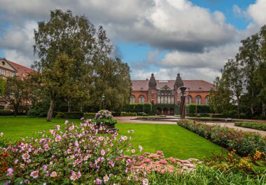 Kopenhag, Danimarka - 14 Eylül 2010: Kraliyet Kütüphanesi 'nin arkasındaki kırmızı tuğlalı Yahudi tarihi müzesi yeşil bahçe ve mavi bulutlar altında çiçek manzarası. Göldeki sütun çeşmesi