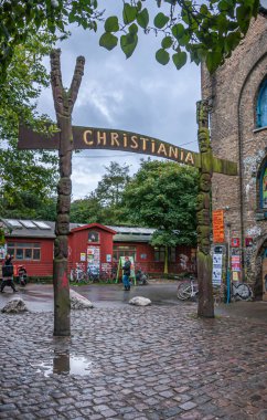 Kopenhag, Danimarka - 14 Eylül 2010: Giriş işareti, kahverengi ahşap üzerinde altın ve Christiania freetown kapısı. Binalar ve arka plandaki insanlar. Biraz yeşil yaprak.