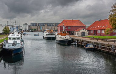 Kopenhag, Danimarka - 14 Eylül 2010: Christianshavn 'daki kanal boyunca gri bulutlar altında tarihi kırmızı askeri binalar. Amiral Oteli, limanın diğer tarafında. Küçük gemiler kenetlendi.