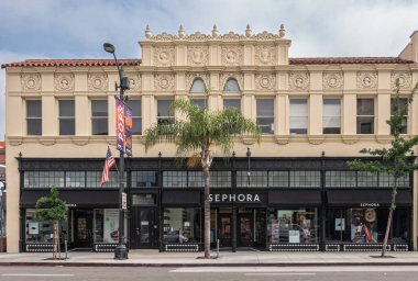 Pasadena, CA, USA - June 8, 2023: Sephora shop, black facade and window on street level of historic beige facade building with mural sculptures under blue cloudscape along Colorado Blvd. clipart