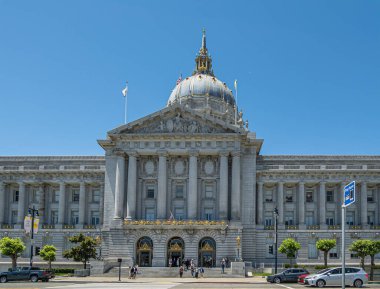 San Francisco, CA, ABD - 12 Temmuz 2023: Gri taş belediye binasının doğu cephesi ve mavi gökyüzünün altındaki dev kubbe. Altın madalyalar kulede ve kulede. Üç bayrak üstte. Yayalar ve arabalar.