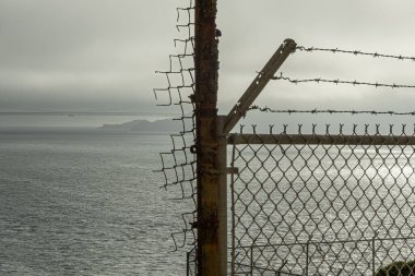 San Francisco, CA, ABD - 12 Temmuz 2023: tarihi Alcatraz hapishanesi. Altın Kapı köprüsü, sisli gecenin bir vakti, dikenli tellerin arkasından gökyüzü.