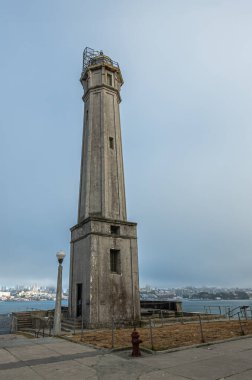 San Francisco, CA, ABD - 12 Temmuz 2023: Tarihi Alcatraz Hapishanesi. Deniz feneri, mavi sisli gökyüzünün altında San Francisco şehir manzarasına yakın..