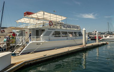 Meksika, Cabo San Lucas - 16 Temmuz 2023: beyaz ve mavi Cabomar feribotu ve tur teknesi mavi gökyüzünün altındaki Greem Water Marina limanına yanaştı. Mevcut insanlar