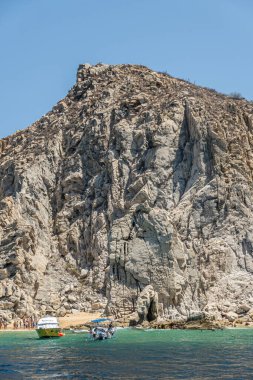 Meksika, Cabo San Lucas - 16 Temmuz 2023: küçük plaj, bol banyo, arazi yakınlarındaki uzun gri kayalık uçurumun altında yeşil körfez suyunda Manta keyif yatı