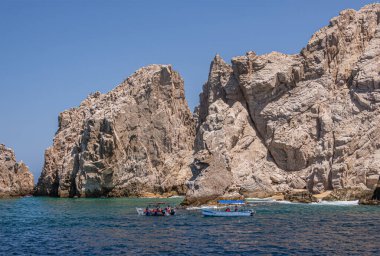 Meksika, Cabo San Lucas - 16 Temmuz 2023 El Arco 'ya mavi gökyüzü altında küçük gezi tekneleri yaklaşıyor. Uzun kayalıklar okyanus suyuna iner.