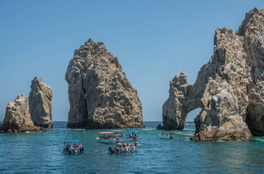 Meksika, Cabo San Lucas - 16 Temmuz 2023: El Arco mavi gökyüzünün altındaki kayalık kayaların ardından ortaya çıktı. Birkaç küçük turist teknesi yeşil suların üzerinde.