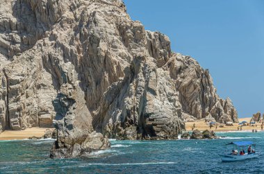 Meksika, Cabo San Lucas - 16 Temmuz 2023 Sandy Beach Playa de los Amantes yarımadanın kayalık kısmındaki mavi gökyüzünün altında görüldü. Yeşil sularda küçük bir turist teknesi