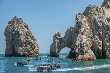 Meksika, Cabo San Lucas, 16 Temmuz 2023, El Arco kayalık kaya yarımadasının doğu ucu mavi gökyüzünün altında. Birkaç küçük turist teknesi yeşil suların üzerinde.