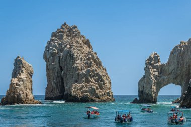 Mexico, Cabo San Lucas - July 16, 2023: El Arco at Reserva de lobos marina, east end of rocky boulder peninsula under blue sky. Several small tourist boats in front on greenish water clipart