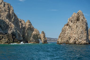 Meksika, Cabo San Lucas - 16 Temmuz 2023: Reserva de Los Marina, El Arco 'da güney manzarası ve yeşil okyanus suyundaki uzun gri kayalar arasında kanal. Şehir manzarası ve ufukta plaj