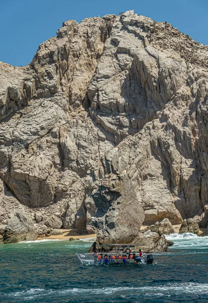 墨西哥 卡波圣卢卡斯 2023年7月16日 在碧眼岩石前的绿水上的玻璃底旅游船 与蓝天下高耸的灰棕色岩石分开 免版税图库图片