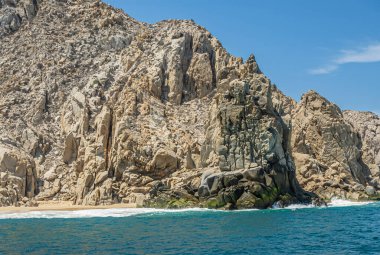 Meksika, Cabo San Lucas - 16 Temmuz 2023 okyanustan Playa de los Amantes sahilinin doğu ucunda kayalık kayalar var. Yeşil okyanus suyunun beyaz dalgaları