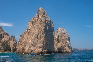 Meksika, Cabo San Lucas - 16 Temmuz 2023: mavi gökyüzünün altındaki mavi okyanus suyundaki en uzak Rezerv De Lobos Marinos kayaları. Ön tarafta küçük gezi tekneleri var. Ufukta şehir manzarası