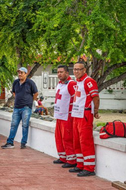 Zihuatanejo, Meksika - 18 Temmuz 2023: 2 ambulans sağlık görevlisi liman iskelesinde kırmızı-beyaz giyinmiş. Arkaplan olarak kırmızı asfalt ve yeşil yapraklar