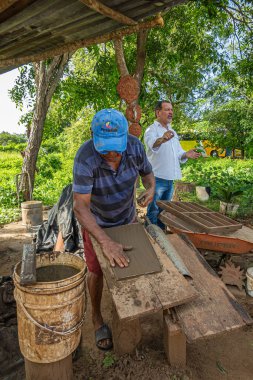 Zihuatanejo, Meksika - 18 Temmuz 2023: Tarihi Terracotta fırını. Çatı penceresi yapmak için kil, özel tezgahta elle düzleştiriliyor. Tercüman arkada. Arkaplan olarak yeşil yapraklar