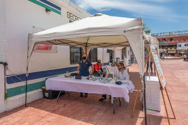 Zihuatanejo, Meksika - 18 Temmuz 2023: Mavi bulutların altında turistlere en popüler ilaçları satan kadınların yer aldığı beyaz çadır