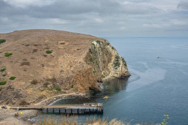 Santa Cruz Adası, CA, ABD - 14 Eylül 2023: Akrep Anchorage iskelesi kaçakçılar yolu boyunca yukarıdan görüldü. Mavimsi okyanusun üzerindeki bulutlar ve uçurumlarla kaplı kahverengi tepeler. Yat görünürde