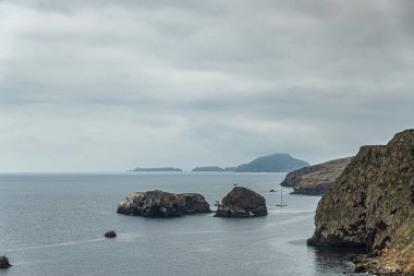 Santa Cruz Adası, CA, ABD - 14 Eylül 2023: Gri bulutlar altında ufukta iki küçük kaya adası ve koyu Anacapa adaları ile NE uçurum kıyı şeridi görüntüsü. Düz okyanus