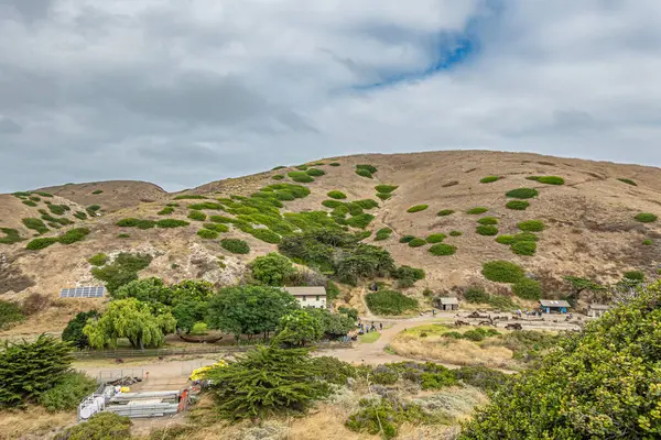 Santa Cruz Adası, CA, ABD - 14 Eylül 2023: Cavern Trail 'in önündeki tarihi Akrep Çiftliği binaları mavi bulutların altındaki tepeyi kaplamıştır. Benekli yeşil bitki örtüsü