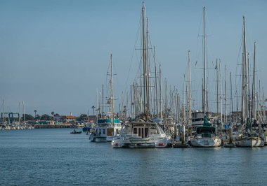 Ventura, CA, ABD - 14 Eylül 2023: Mavi gökyüzünün altında bir gemi direği var. Motor ve yelkenli tekneleri rıhtımlarına yanaşmış, ufuktaki binalar. mavi gökyüzü ve su