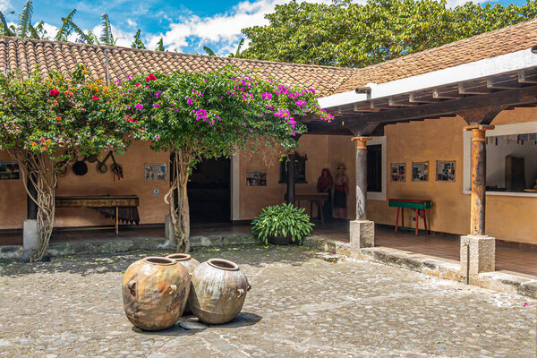 Guatemala, La Antigua - July 20, 2023: Finca La Azotea museums. Central courtyard surrounded by one level exhibition buildings. Flowers and green foliage under blue cloudscape