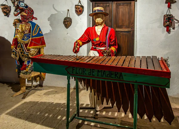 Guatemala, La Antigua - 20 Temmuz 2023 Finca La Azotea müzeleri. Erkek bebek büyük tarihi bir ksilofon enstrümanı çalıyor. Beyaz duvara doğru yaklaşın. Geleneksel giyinmiş kadın bebek.