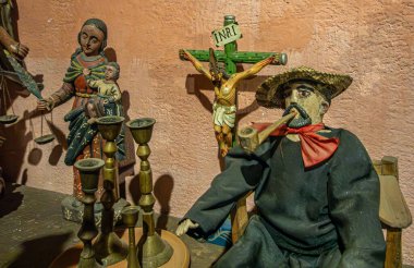 Guatemala, La Antigua - 20 Temmuz 2023 Finca La Azotea müzeleri. Sigara içen adam heykeli, çarmıhta İsa 'nın heykeli ve arkada bebeği olan Meryem Ana, yakın plan.