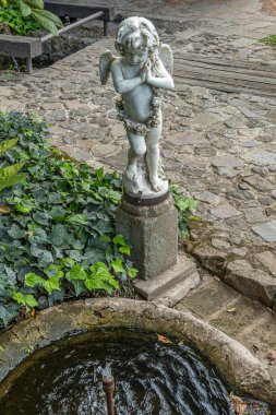 Guatemala, La Antigua - 20 Temmuz 2023 Casa Santa Domingo Müzesi. Bahçedeki küçük beyaz melek heykeli çeşmenin önünde ve yeşil yapraklar ve gri taş kaldırımlarla çevrili.