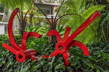 Guatemala, La Antigua - 20 Temmuz 2023 Casa Santa Domingo Müzesi. Yeşil yapraklı kan kırmızısı modern sanat. Gövde ve tekerlekler