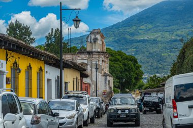 Guatemala, La Antigua - 20 Temmuz 2023 Calle del Hermano Pedro 'dan güneye, mavi bulutların altındaki yeşil volkan dağına, arabalı Cityscape' e bakıyorum. La Conception kilisesi harabesi