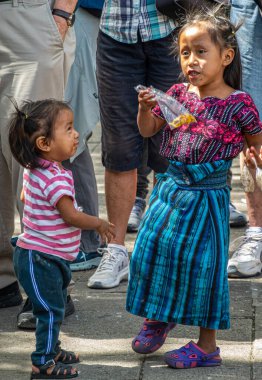 Guatemala, La Antigua - 20 Temmuz 2023: Meydan Belediye Başkanı Meydanı 'nda yeni yürümeye başlayan bebekle birlikte renkli geleneksel giysiler içindeki genç kız