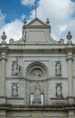 Guatemala, La Antigua - 20 Temmuz 2023: Üzerinde Meryem 'in 6 heykeli, Tanrı' nın kendisi, havarileri ve mavi bulutlar altındaki azizlerin bulunduğu bedavaya beyaz ön cepheye yakın çekim
