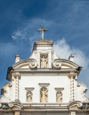 Guatemala, La Antigua - 20 Temmuz 2023: Portre, San Francisco el grande Kilisesi, azizin heykelleri ve müritlerinin heykeli ile ön cephedeki en üst beyaz taş bölümünün yakın çekimi. Mavi bulut