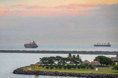 Guatemala, Puerto Quetzal - 20 Temmuz 2023: Akşam gökyüzü. Playa La Caleta 'nın güneş sığınakları ve yeşil yaprakları var. 1 konteynır gemisi ve 1 gemi limana girmeden önce okyanusta bekliyor.