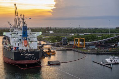 Guatemala, Puerto Quetzal - 20 Temmuz 2023: Unity Endeavour hangarının üzerinde gün batımı gökyüzü. Uzun nakliye kemeri ve birkaç yat. Yeşil yeşillik kemeri