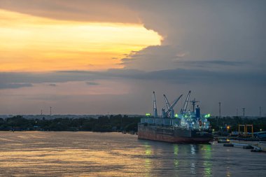 Guatemala, Puerto Quetzal - 20 Temmuz 2023: Birlik Endeavour kömür gemisi üzerine gece çöktü. Yeşil kuşak manzarası. Taşıyıcıdaki ışıklar ve bulutların arasından süzülen sıcak güneş ışınları