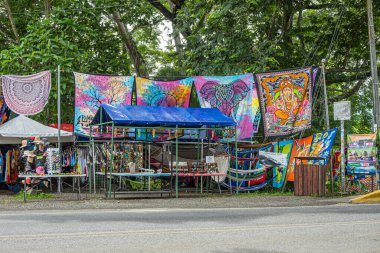 Kosta Rika, Luganillas - 22 Temmuz 2023: Tarcoles Nehri ve Timsah Köprüsü perakende şirketleri. Yeşil yaprakların altında moda ve Hindu temalı tekstil mağazası. Masa kıyafetleri, herkes için elbiseler, şapkalar ve daha fazlası sergileniyor.