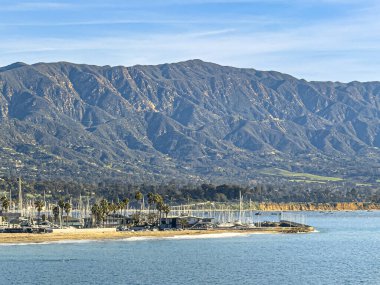 Santa Barbara, CA, ABD - 28 Ocak 2024: Liman Rıhtımı ve Castillo Point ile güney tarafı. Beyaz tekne direği koleksiyonu. Mavi bulutların altında dağ sıraları
