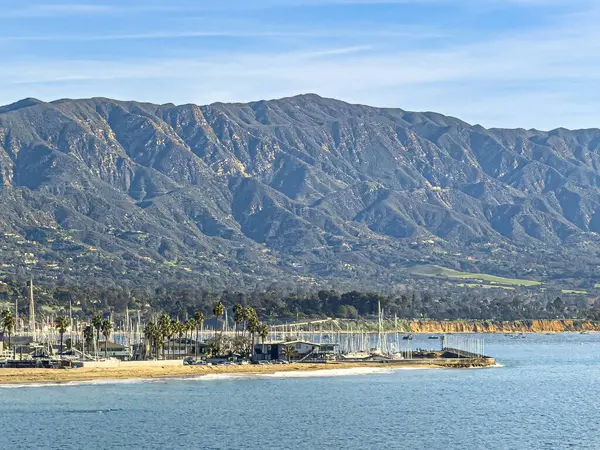 Santa Barbara, CA, ABD - 28 Ocak 2024: Liman Rıhtımı ve Castillo Point ile güney tarafı. Beyaz tekne direği koleksiyonu. Mavi bulutların altında dağ sıraları