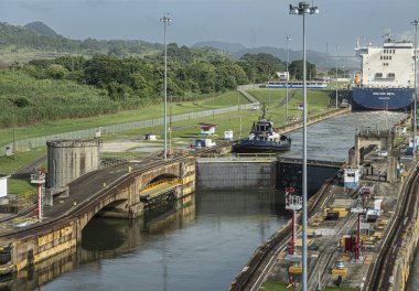 Panama Kanalı, Panama - 24 Temmuz 2023: Miraflores, römorkör ve CMA CGM Neva konteynır gemisi ile sol odaya açılan kapıları kilitledi. Mavi gökyüzünün altındaki yeşil manzara
