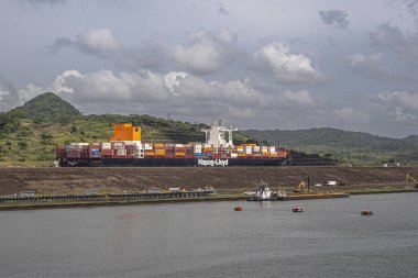 Panama Kanalı, Panama - 24 Temmuz 2023: Hapag-Lloyd konteyner gemisi yeni Pedro Miguel 'in kuzeyinde gri bulutların altında kilitli. Konteynırlar renk ekler. Sahil şeridinde çalışma devam ediyor