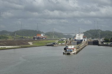 Panama Kanalı, Panama - 24 Temmuz 2023: Pedro Miguel Centennial köprüsü, Pan-Amerikan otoyol köprüsü arkasında gri bulutların altında kaldı. Yeşil tepeli geniş bir manzara. Konteyner gemileri