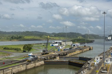 Panama Kanalı, Panama - 24 Temmuz 2023: Pedro Miguel 'in çıkış kapıları mavi bulutların altında kilitlenir. Yeşil orman kıyıları, ufukta konteyner gemisi