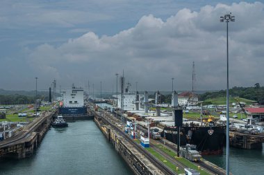 Panama Kanalı, Panama - 24 Temmuz 2023: Gatun mavi bulutların altında Atlantik tarafında kilitleniyor. CMA CGM konteynır gemisi ayrılıyor, Nord Bering hangar taşıyıcısı giriyor