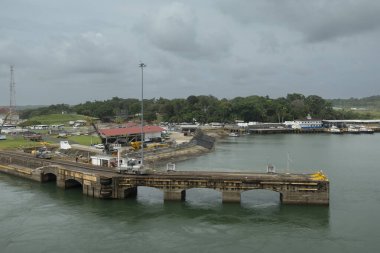 Panama Kanalı, Panama - 24 Temmuz 2023: Gatun 'un doğu rıhtımı, Panama Kanalı tarafında gri bulutların altında. Makineler ve gemi traktörleri. Yeşil ormanlık kıyı şeridi arkada.