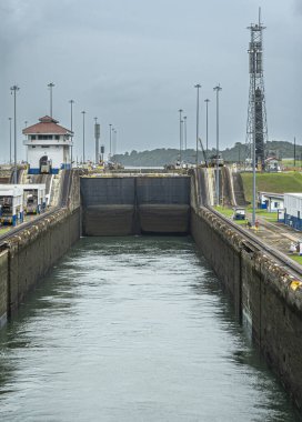 Panama Kanalı, Panama - 24 Temmuz 2023: Gatun 'da Atlantik' e giden 2. odayı kilitliyor. Gözcü binası ve ilk odanın kapalı kapıları. Yukarıda, mavi bulutların altında görünür bir kanal var. Çekiciler ve makineler
