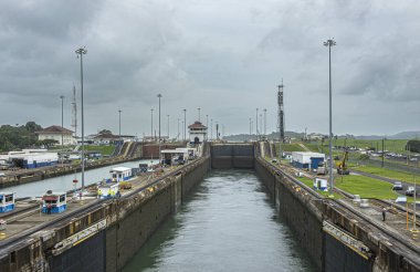 Panama Kanalı, Panama - 24 Temmuz 2023: Gatun kilitleri batıya bakıyor, bir oda temizlendi, aşağı iniyor, gri bulutlar altında. Küçük binalar ve bir sürü makine, ışıklar ve gözetleme kulesi.