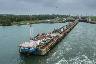 Panama Kanalı, Panama - 24 Temmuz 2023: Gatun gri-mavi gökyüzü altında Atlantik sularına doğru genişleyen ana iskeleyi kilitler. Yeşil kuşak ufukta. Gemi traktörlerini hizaya soktu